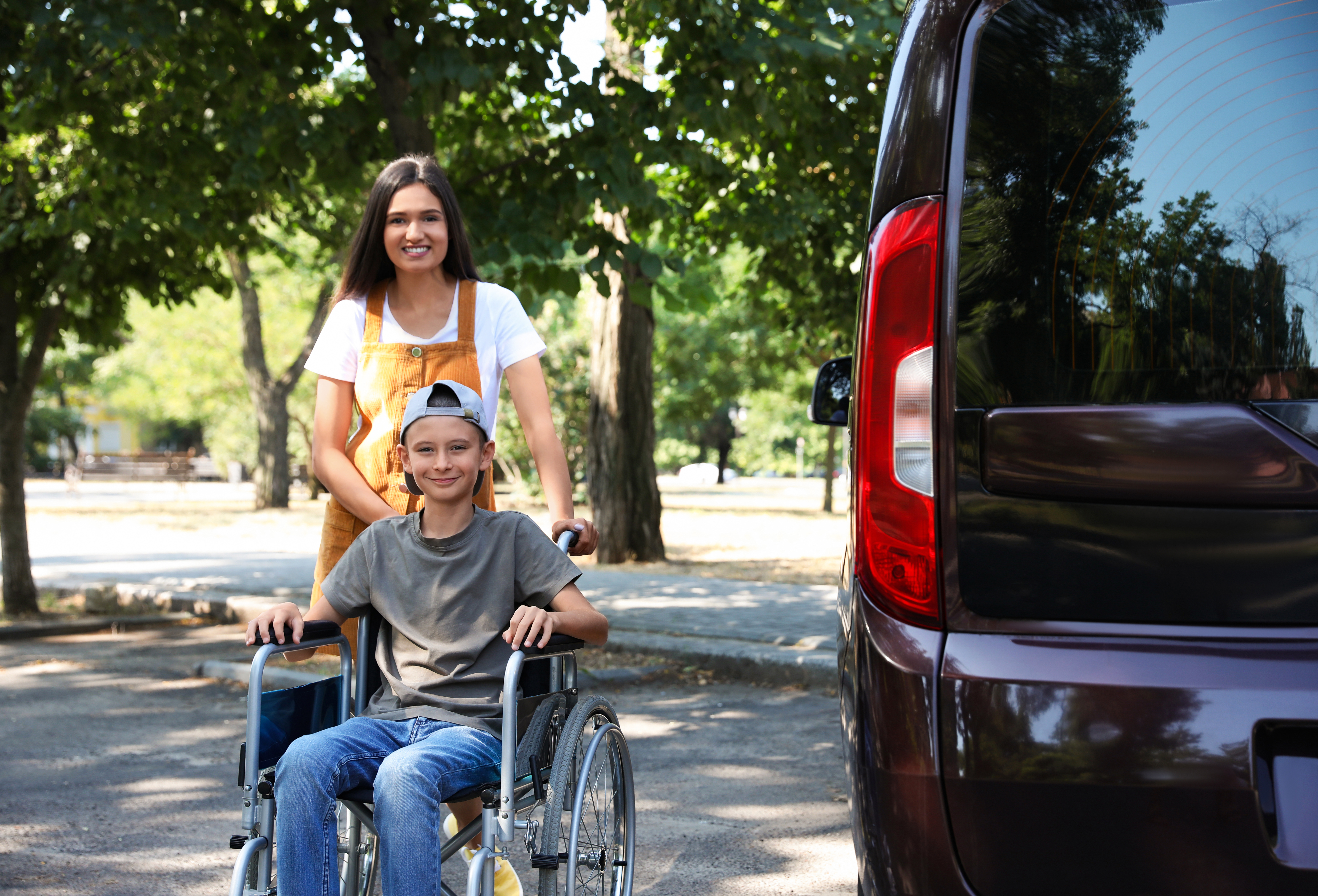 an expert NEMT driver next to a wheelchair-accessible car and her disabled passenger